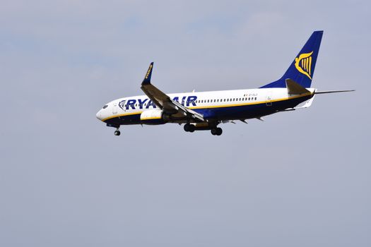 Vertrekbord op luchthaven met Ryanair-vluchten en reizigers die prijzen vergelijken op hun telefoon